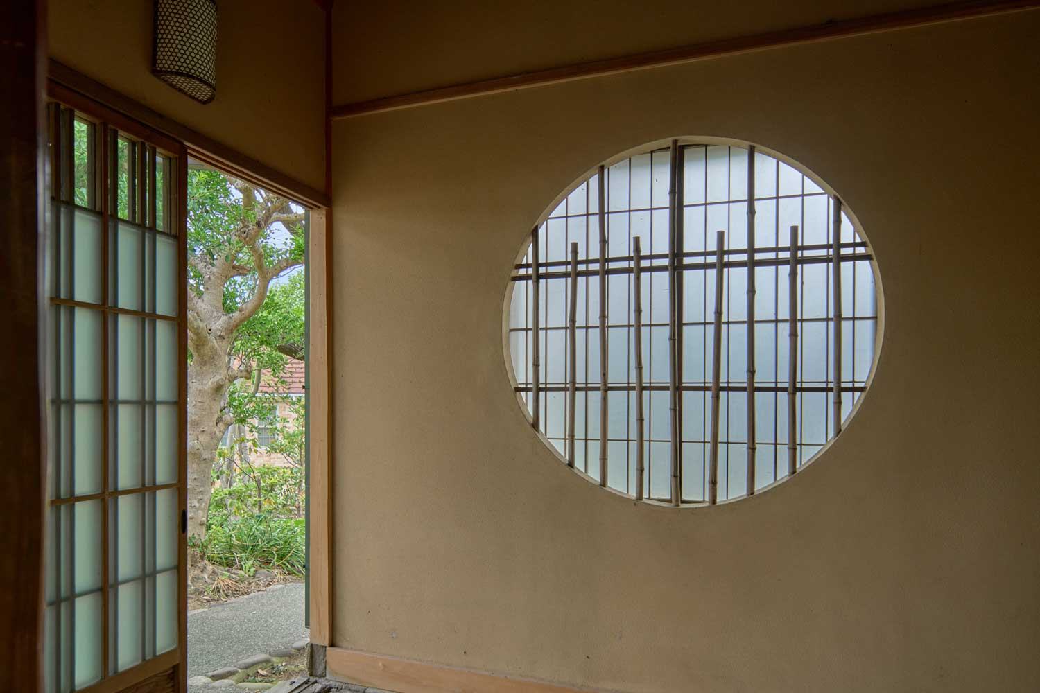 丸窓と障子のある玄関土間。三和土の床が広がる。