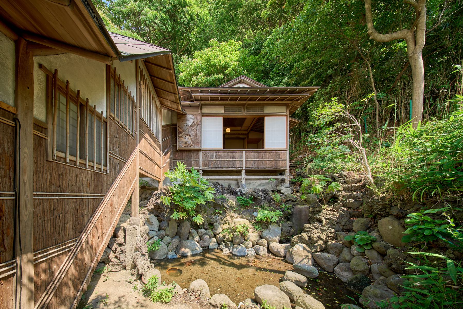 母屋から池を隔てて佇む離れ。石を組んだ流れと深い緑に囲まれている。